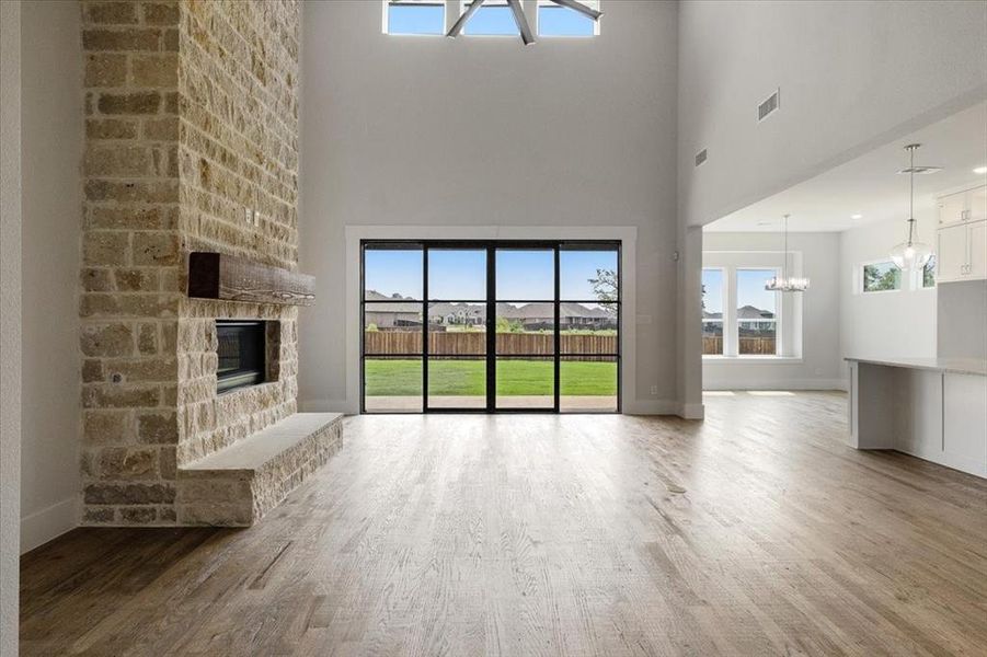 Unfurnished living room featuring brick wall, an inviting chandelier, hardwood / wood-style floors, a stone fireplace, and a high ceiling