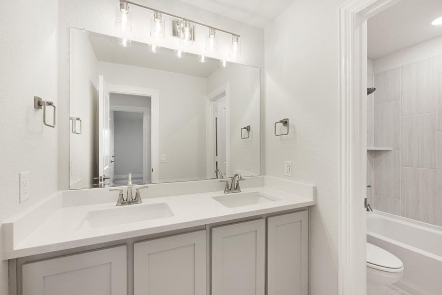 Bathroom with double sink vanity, gray cabinets, white countertop, and tiled shower-tub combo