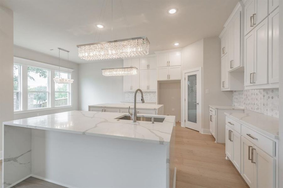 Kitchen with light stone countertops, a kitchen island with sink, white cabinetry, recessed lighting, and decorative backsplash