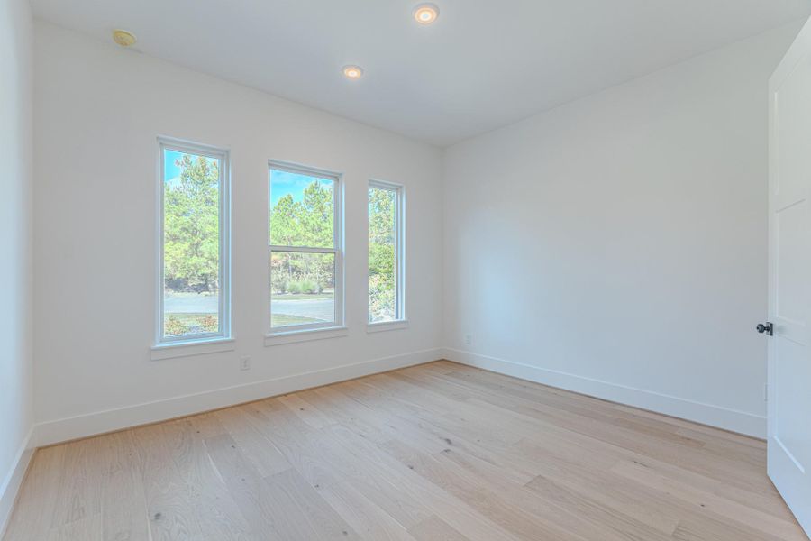 Bright room with light wood flooring and three large windows offering a scenic view of greenery. The space has neutral walls, recessed lighting, and a modern, clean look. Ideal for a bedroom or office.