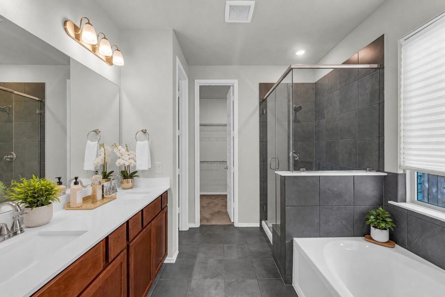 This primary bathroom showcases a double vanity with an integrated white countertop, a soaking tub, and a separate walk-in shower wrapped in dark gray tile. This primary bathroom showcases a double vanity with an integrated white countertop, a soaking tub, and a separate walk-in shower wrapped in dark gray tile.