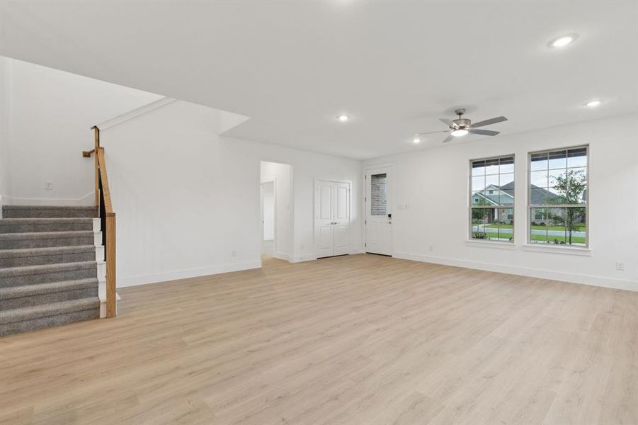 Unfurnished living room with ceiling fan, light wood-type flooring, recessed lighting, and stairs Unfurnished living room with ceiling fan, light wood-type flooring, recessed lighting, and stairs