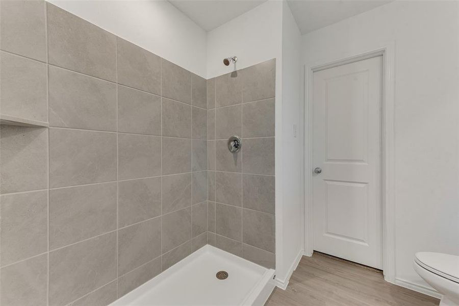 Bathroom featuring toilet, hardwood / wood-style floors, and a tile shower