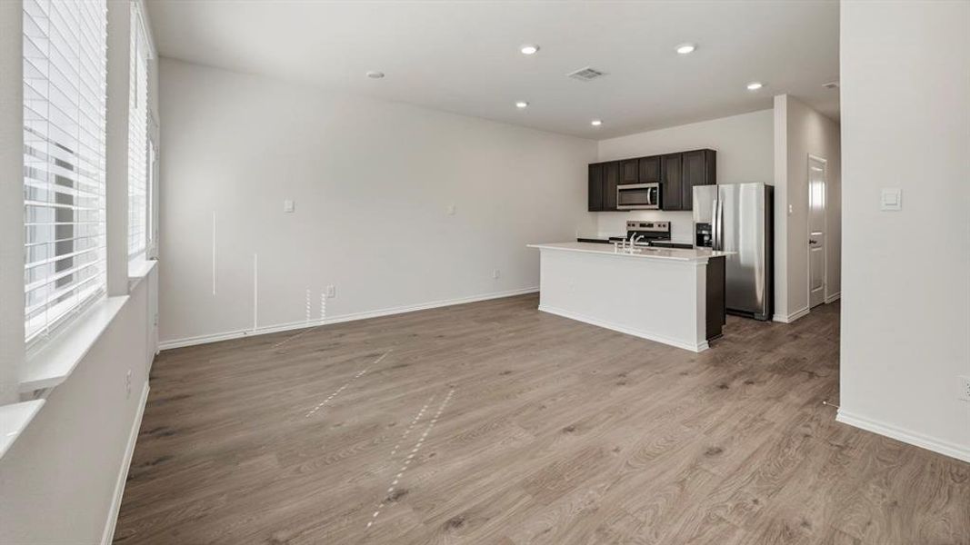 Kitchen featuring an island with sink, appliances with stainless steel finishes, light wood-style flooring, open floor plan, and recessed lighting