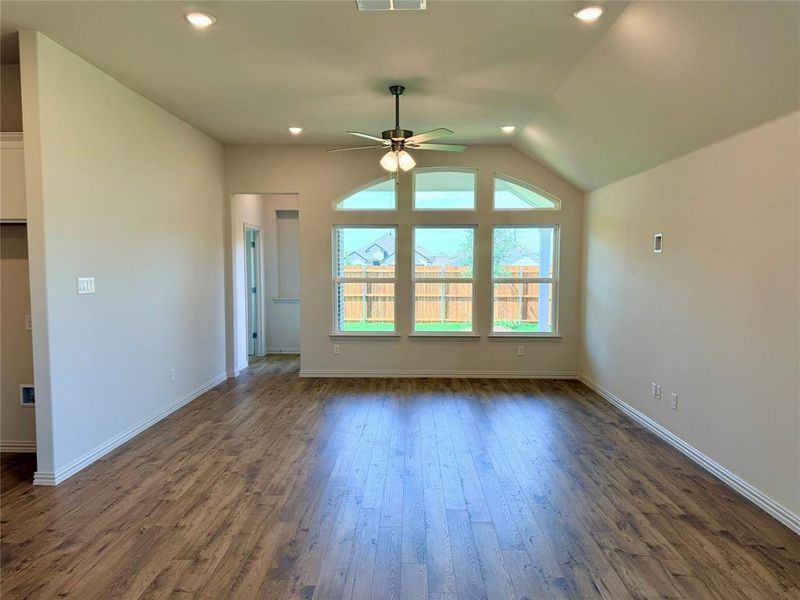 Spacious room featuring vaulted ceilings, wood-finish flooring, and a large window array with an arched transom