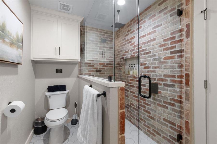 Bathroom featuring a shower stall, light tile patterned flooring, and brick wall Bathroom featuring a shower stall, light tile patterned flooring, and brick wall