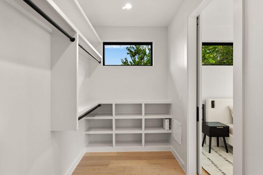 Custom shelving and hanging rods organize this walk-in closet featuring light wood flooring.