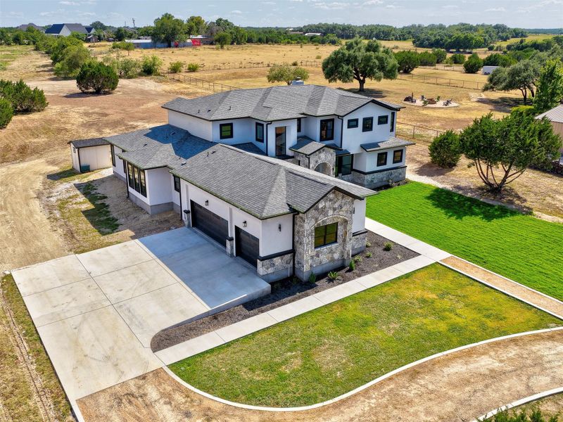 An aerial perspective showcases a sprawling modern home with a concrete driveway and stone accents.