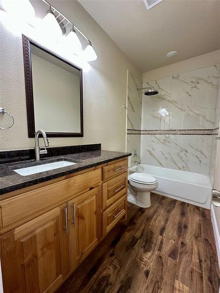 Full bathroom featuring wood-type flooring, tiled shower / bath combo, vanity, and toilet