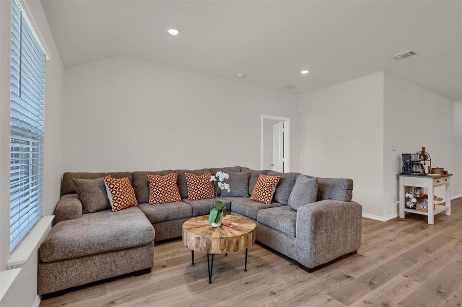 Living area featuring lofted ceiling, light wood-style flooring, baseboards, visible vents, and recessed lighting