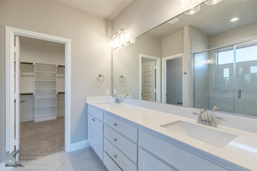 Bathroom featuring double vanity, a walk in closet, light marble finish floors, and a marble finish shower