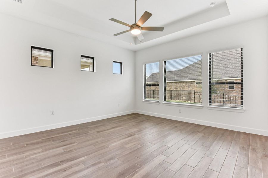 Unfurnished room with a tray ceiling, light wood finished floors, and a ceiling fan Unfurnished room with a tray ceiling, light wood finished floors, and a ceiling fan