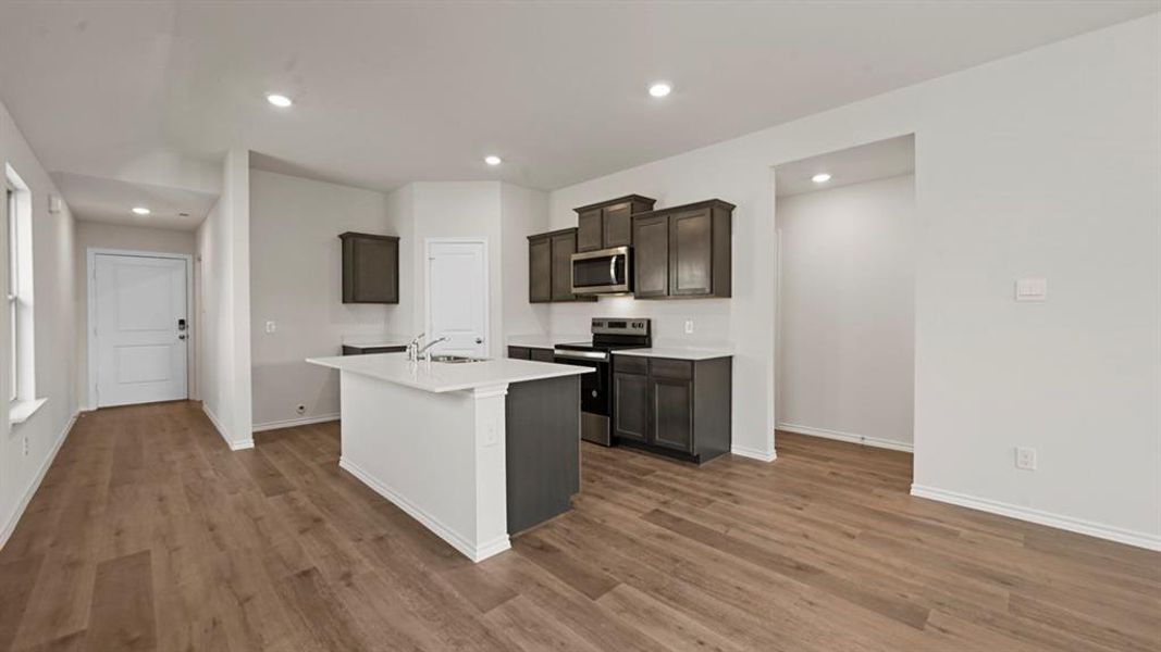 Kitchen featuring stainless steel appliances, an island with sink, recessed lighting, dark wood finish cabinetry, and dark wood-type flooring
