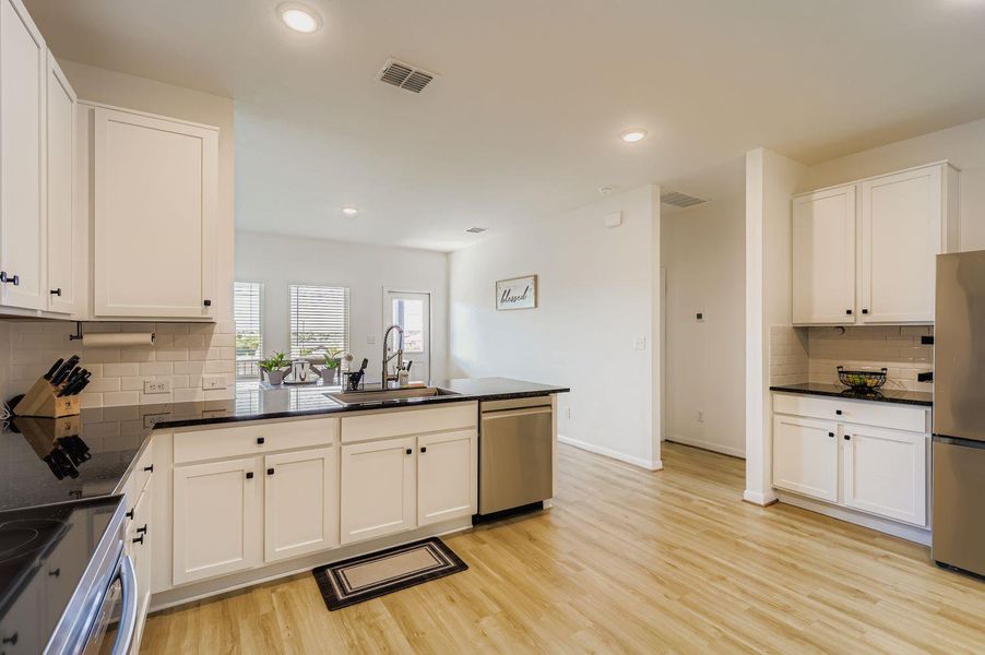 Kitchen with tasteful backsplash, appliances with stainless steel finishes, a peninsula, white cabinetry, and recessed lighting