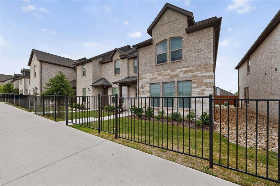 This property features a brick and stone exterior, visible windows, and a well-maintained lawn area behind a black metal fence