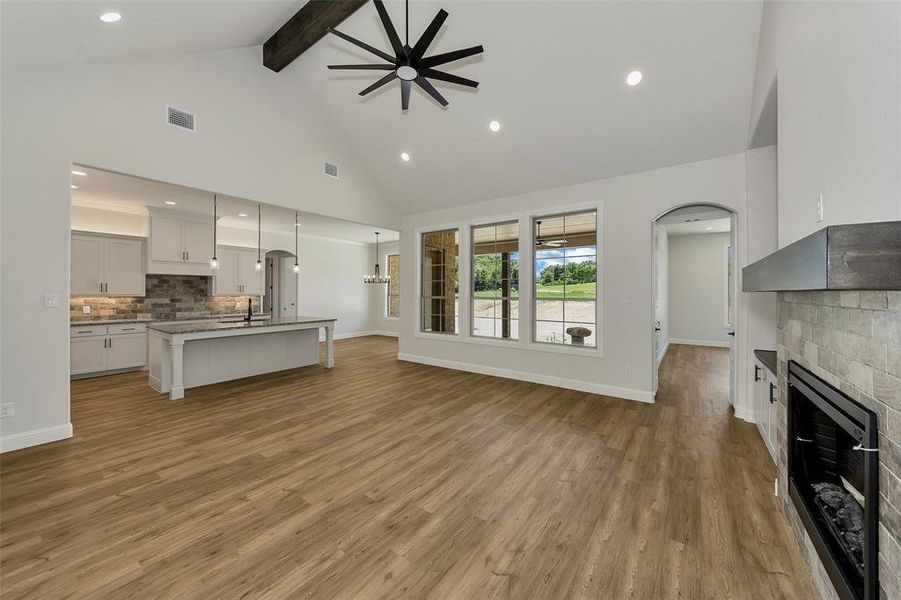 Living room featuring arched walkways, a fireplace, high vaulted ceiling, light wood-style floors, and beam ceiling