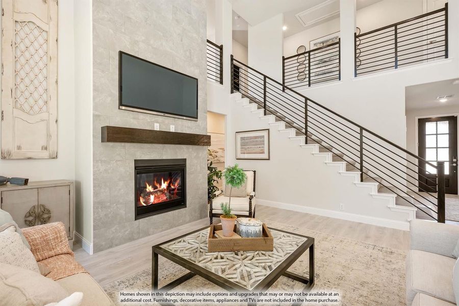 Two-story living room with tile fireplace, wall-mounted TV, and open staircase with metal railing