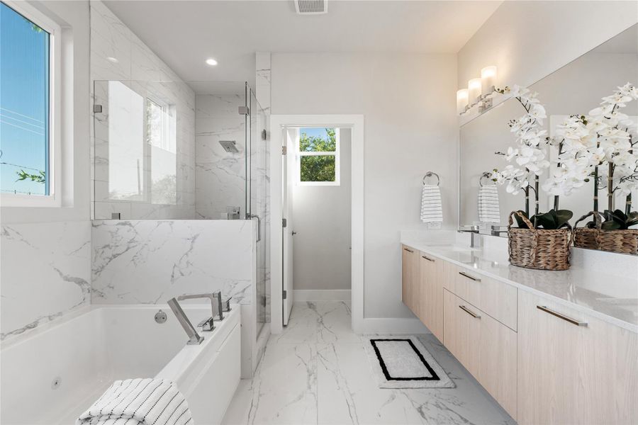 Spa-like primary bath featuring a floating double vanity, soaking tub & frameless glass shower all wrapped in elegant marble-inspired tile for a clean, modern finish. Spa-like primary bath featuring a floating double vanity, soaking tub & frameless glass shower all wrapped in elegant marble-inspired tile for a clean, modern finish.