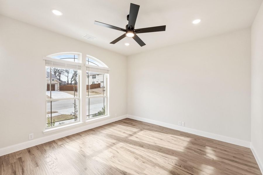 Empty room with light wood floors, black ceiling fan, and arched windows overlooking a neighborhood street