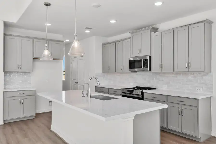 Stunning pendant lighting, beautiful cabinetry, and a stylish backsplash!