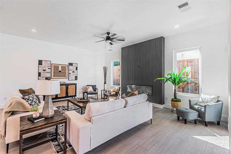 Living room with plenty of natural light, light wood-style floors, a large fireplace, ceiling fan, and recessed lighting Living room with plenty of natural light, light wood-style floors, a large fireplace, ceiling fan, and recessed lighting