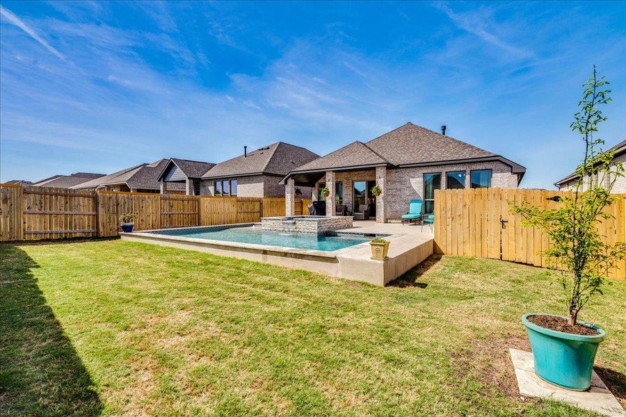 Rear view of property featuring a patio, brick siding, a fenced backyard, a shingled roof, and a pool with connected hot tub