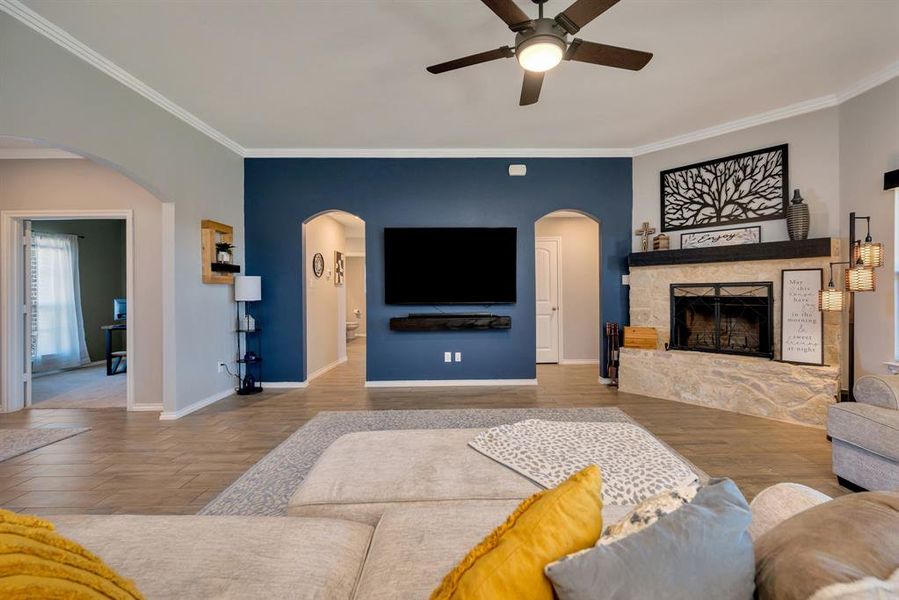 Living room featuring wood finished floors, ceiling fan, a fireplace, ornamental molding, and arched walkways