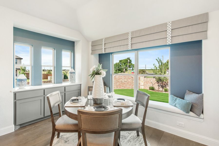 Breakfast nook with round dining table, window seat, and large windows overlooking backyard