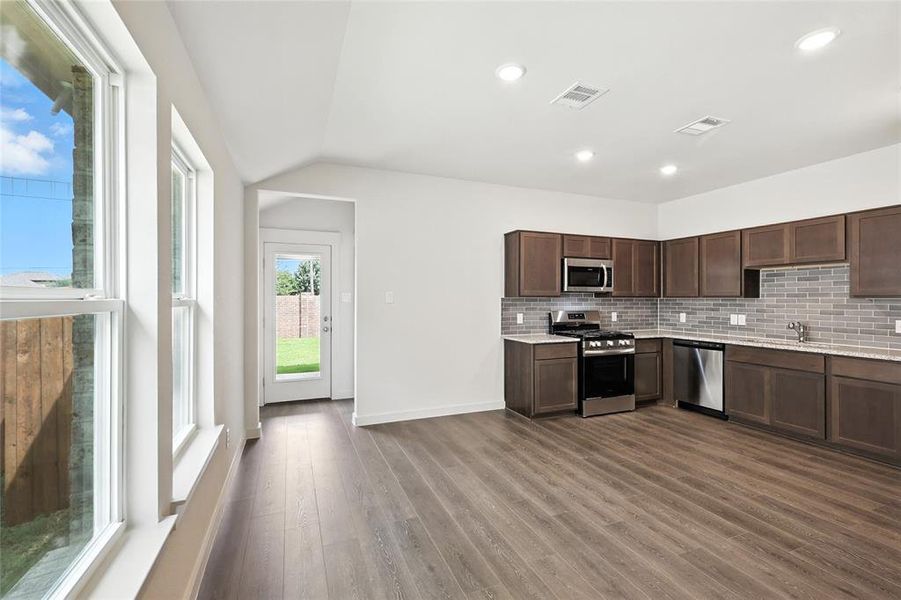 Kitchen with stainless steel appliances, light countertops, decorative backsplash, wood finished floors, and lofted ceiling Kitchen with stainless steel appliances, light countertops, decorative backsplash, wood finished floors, and lofted ceiling