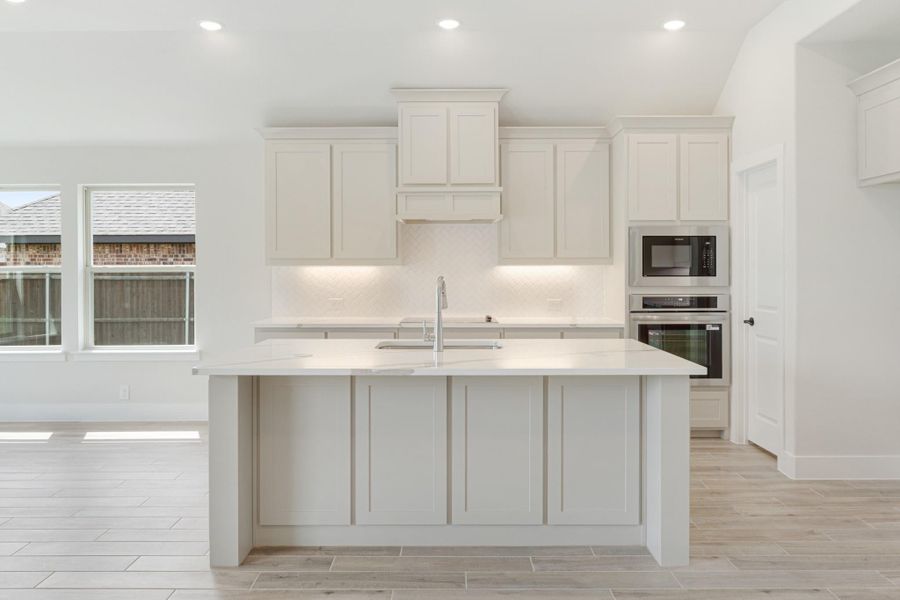 White kitchen with large island, quartz countertops, herringbone backsplash, and stainless steel built-in appliances