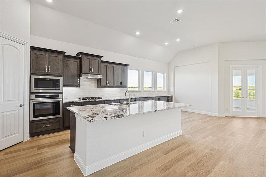 Kitchen with stainless steel appliances, lofted ceiling, recessed lighting, decorative backsplash, and light stone countertops