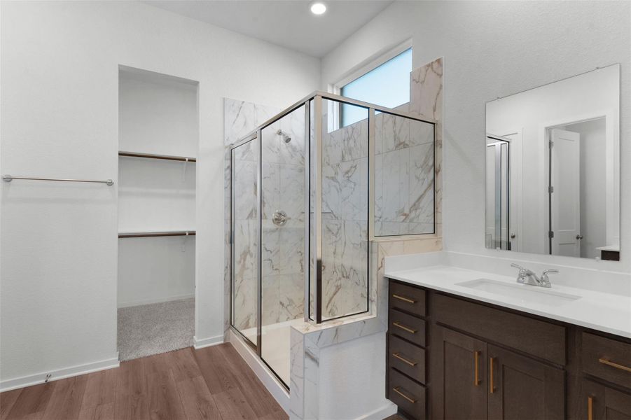 Full bath featuring a spacious closet, light wood finished floors, vanity, and a marble finish shower