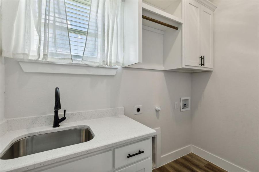 Utility room featuring a stainless steel sink, a dark finish faucet, white cabinetry with dark hardware, solid surface countertops, and wood-finish flooring