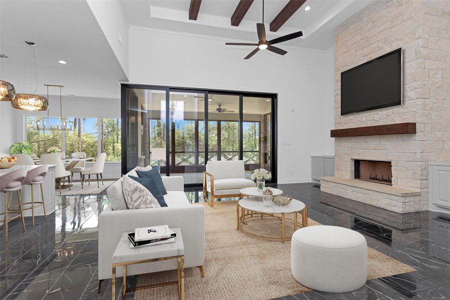 The open-concept living area impresses with soaring ceilings, exposed wood beams, a striking stone fireplace, and seamless indoor-outdoor flow through expansive glass sliders overlooking the wooded landscape.
