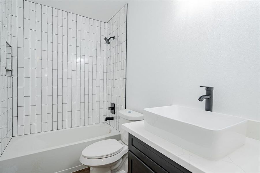 Full bathroom featuring tiled shower / bath combo, toilet, and vanity