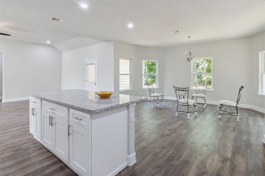 This open-concept living space features a spacious kitchen. The dining area is bright with multiple windows and stylish light fixtures, complemented by elegant flooring throughout.