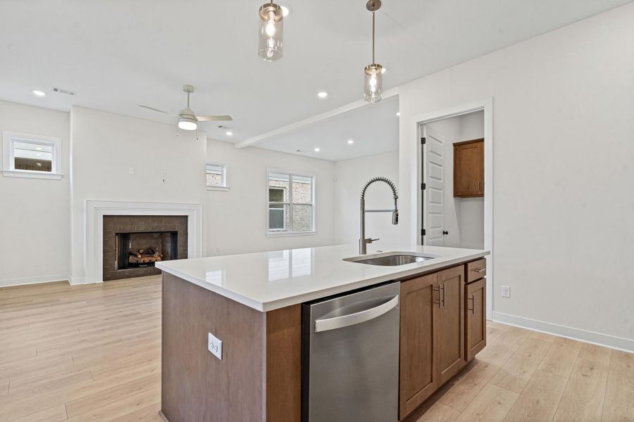 Kitchen island with light wood-finish cabinetry, a stainless steel dishwasher, and a white countertop Kitchen island with light wood-finish cabinetry, a stainless steel dishwasher, and a white countertop