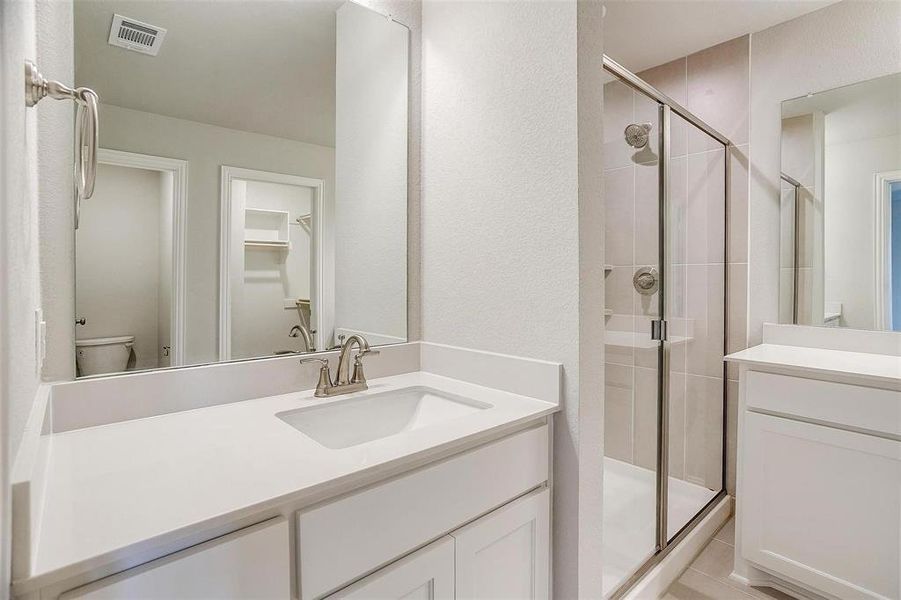 Full bathroom featuring a stall shower, vanity, a textured wall, and a spacious closet Full bathroom featuring a stall shower, vanity, a textured wall, and a spacious closet