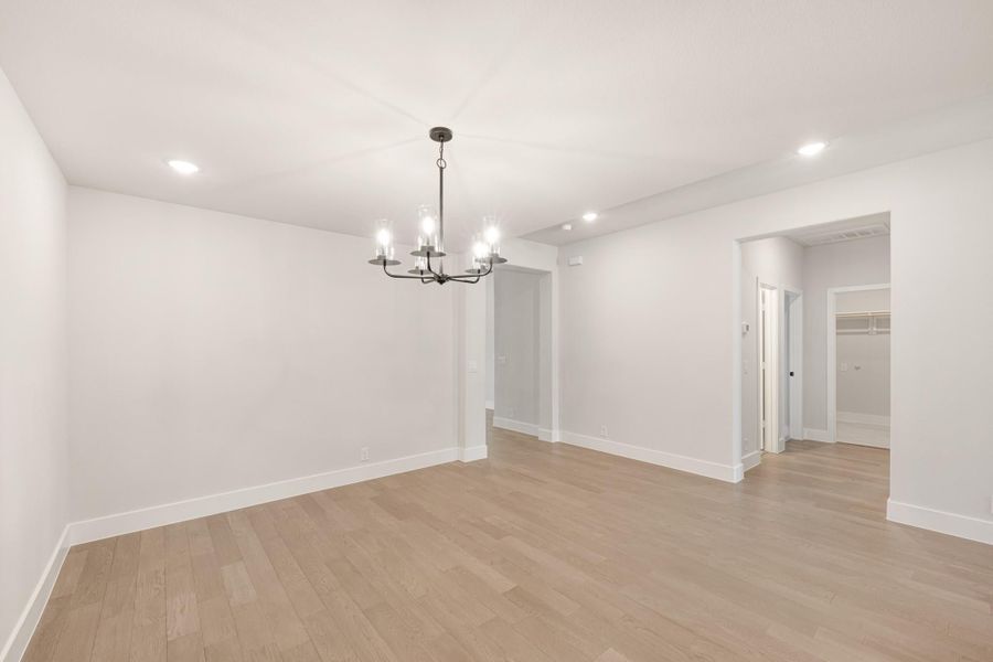 Empty dining room with light hardwood floors, white walls, and a black chandelier overhead