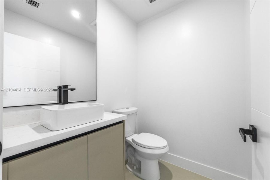 Vanity featuring a rectangular vessel sink, quartz countertop, matte black faucet, and frameless mirror, paired with a two-piece toilet and matching matte black hardware