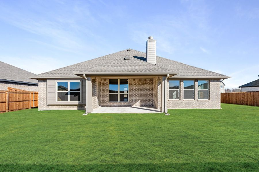 Rear exterior of single-story brick home with covered patio, chimney, and fenced backyard with green lawn