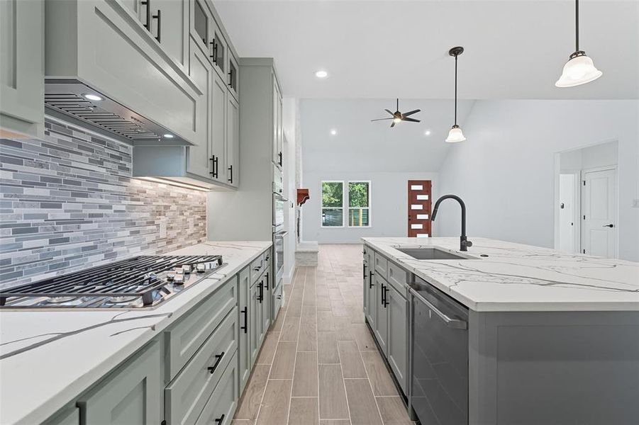 Kitchen featuring lofted ceiling, gray cabinets, light stone counters, range hood, and decorative light fixtures Kitchen featuring lofted ceiling, gray cabinets, light stone counters, range hood, and decorative light fixtures