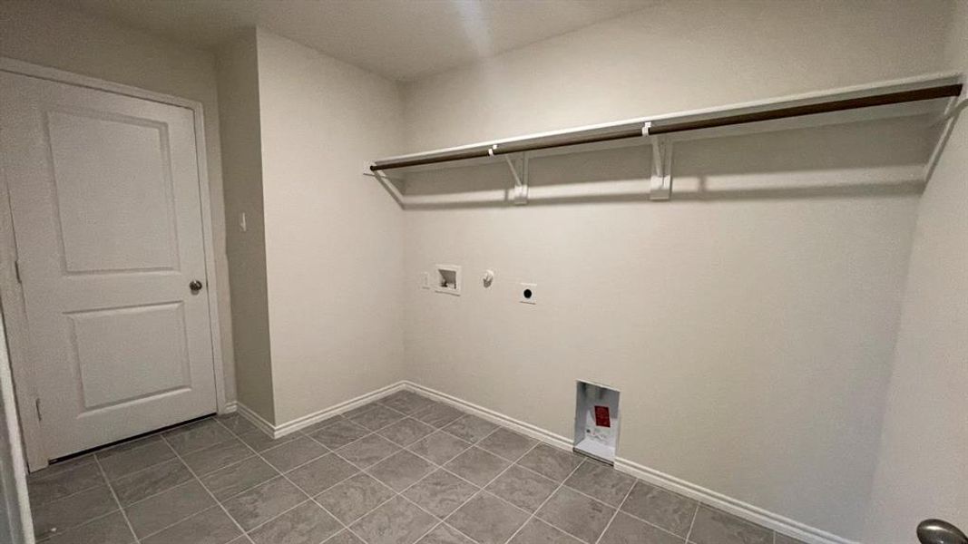 Dedicated laundry area featuring a white two-panel door, gray square tile flooring, a wall-mounted shelving unit, and utility connections Dedicated laundry area featuring a white two-panel door, gray square tile flooring, a wall-mounted shelving unit, and utility connections
