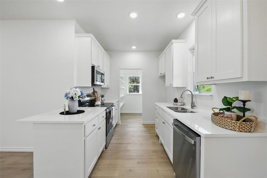 Kitchen with stainless steel appliances, a sink, baseboards, white cabinetry, and light wood-type flooring Kitchen with stainless steel appliances, a sink, baseboards, white cabinetry, and light wood-type flooring