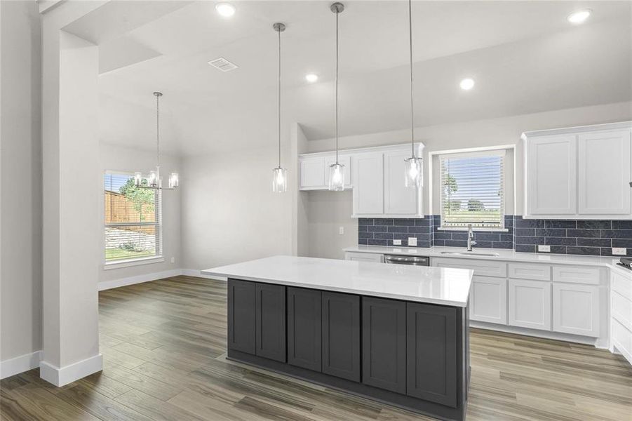Kitchen featuring a quartz-topped island with dark cabinetry, white perimeter cabinetry, dark subway tile backsplash, and wood-finish flooring Kitchen featuring a quartz-topped island with dark cabinetry, white perimeter cabinetry, dark subway tile backsplash, and wood-finish flooring