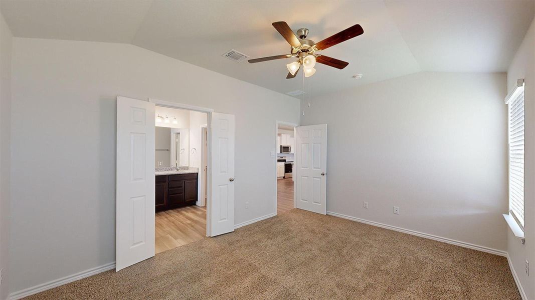 Unfurnished bedroom featuring lofted ceiling, light carpet, ceiling fan, and ensuite bathroom