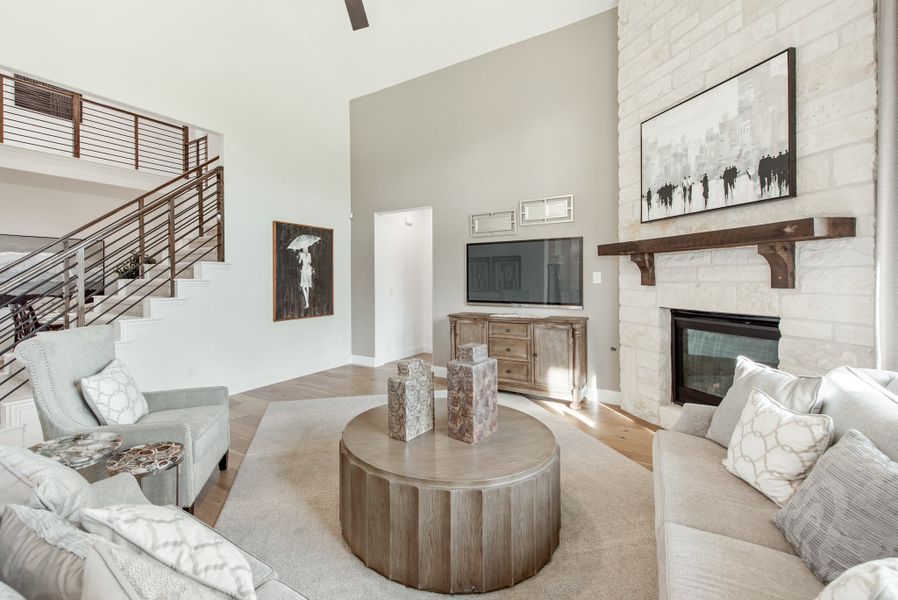 Living room with vaulted ceiling, stone fireplace, round wood coffee table, and open staircase with metal railing