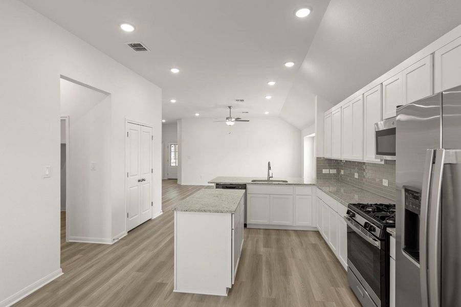 Kitchen with appliances with stainless steel finishes, white cabinets, a kitchen island, vaulted ceiling, and light wood finished floors