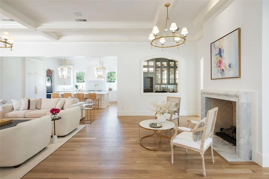 Living room featuring a high end fireplace, beamed ceiling, light wood flooring, and an inviting chandelier