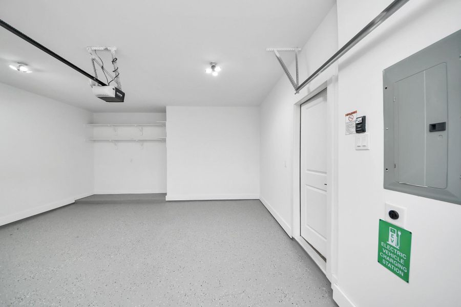 This photo shows a clean, spacious garage with epoxy floor, white walls, and ceiling lights. It features built-in shelving, an electric vehicle charging station, and a garage door opener. Ideal for parking and storage. This photo shows a clean, spacious garage with epoxy floor, white walls, and ceiling lights. It features built-in shelving, an electric vehicle charging station, and a garage door opener. Ideal for parking and storage.